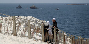 Zwei menschen am Meer, im Hintergrund sind Patrouillenboote zu sehen