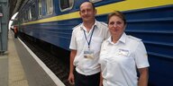 Ein Mann und eine Frau stehen in Dienstkleidung der Zugbegleitung vor einem blauen Zug mit gelbem Streifen