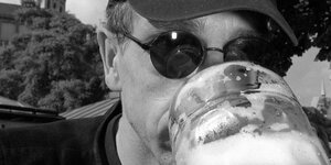 Schwarzweiß Porträt eines Mannes mit Cappy, Sonnenbrille und einem Bierhumpen vor dem Gesicht