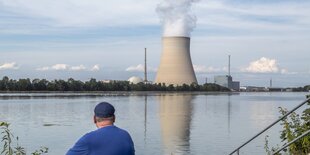 mann sitzt vor Fluss, im HIntergrund AKW-Kühlturm