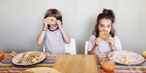 Zwei Kinder am Esstisch machen Faxen mit Brot