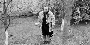 Eine alte Frau mit Kopftuch steht zwischen Bäumen