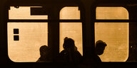 Silhoutten von drei menschen, die am frühen Morgen in einer stadtbahn sitzen