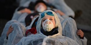 Menschen protestieren in weißer Schutzkleidung. Jemand hat auf seine Mundschutzmaske die Worte "Stop Ceta" geschrieben