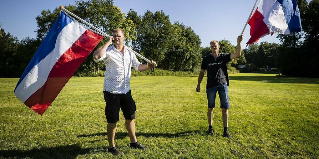 Zwei Männer auf einer großen Wiese schwenken riesige Fahnen in den Farben blau-weiß-rot