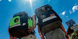 Zwei Kinder mit Schulranzen gehen bei sonnigem Himmel spazieren