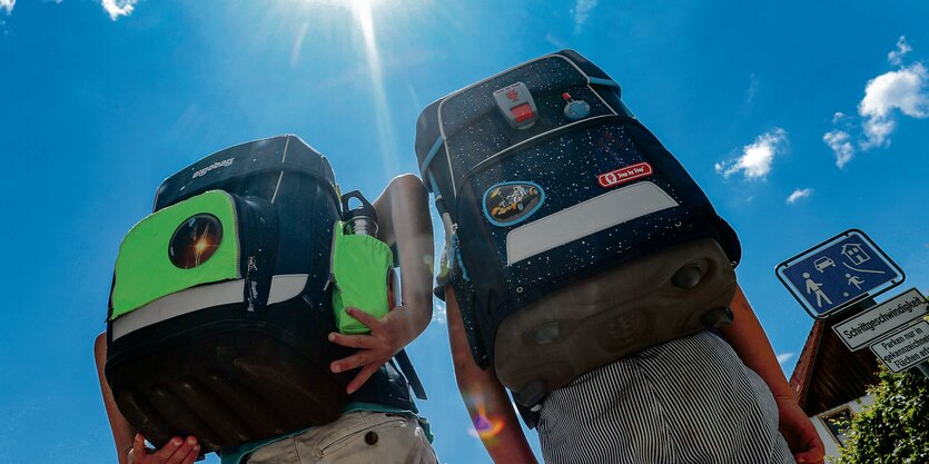 Zwei Kinder mit Schulranzen gehen bei sonnigem Himmel spazieren