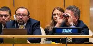 Zwei Männer im Vordergrund, einer sieht auf einen Laptop, der andere sieht durch einen Feldstecher: das ist der ukrainische UN-Botschafter Serhij Kyslytsya