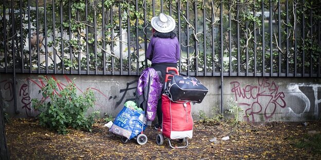 Eine obdachlose Frau steht vor einem Zaun