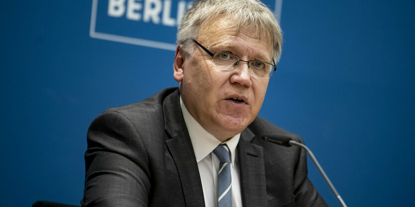 Ein Mann sitzt auf einer Pressekonferenz auf dem Podium