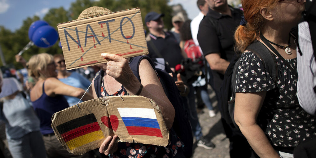 Eine Frau hält zwei Pappschilder für Russland hoch