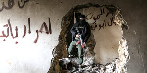 Ein vermummter Kämpfer mit einem Maschinengewehr - fotografiert durch ein Loch in der Wand einer Hausruine