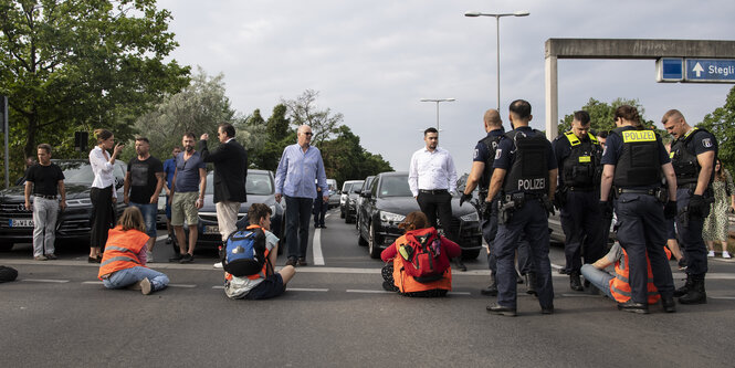 Straßenblockade der Letzten Generation. Autofahrer sind ausgesteigen und stehen ihnen gegebüber. Auch Polizisten sind da