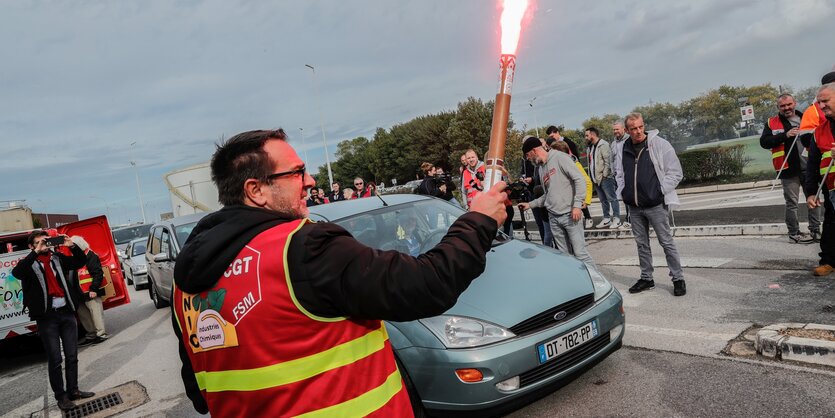 Ein Mann mit Warnweste neben einem Auto hält ein brennendes Bengalo in der Hand