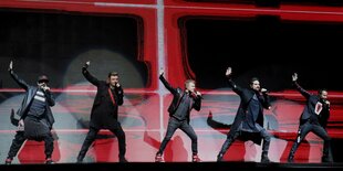 5 Backstreet Boys tanzen auf einer bühne mit rot-schwarzem Hintergrund