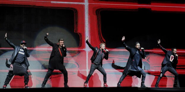 5 Backstreet Boys tanzen auf einer bühne mit rot-schwarzem Hintergrund