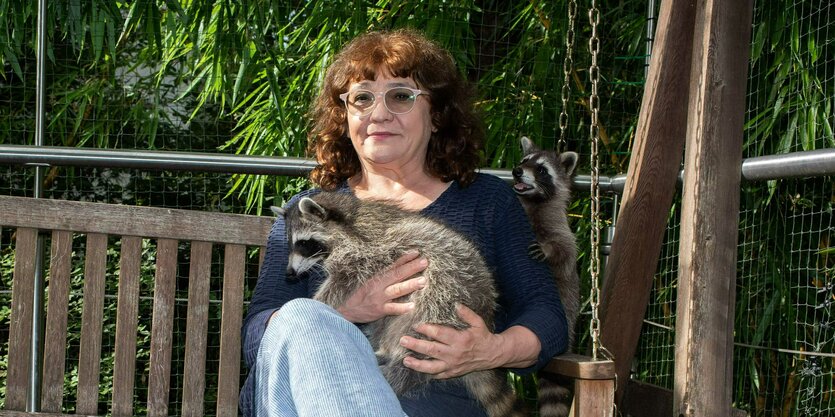 Eine sitzende Frau mit einem Waschbären auf dem Schoß