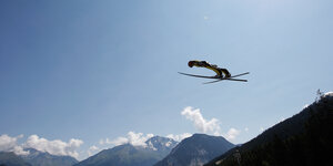 Ein Skispringer im Flug, dahinter Berge und strahlendblauer Himmel