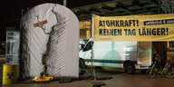 Ein aufblasbares AKW mit Rissen und Pflastern steht vor einer Halle, auf dem Transparent steht: Atomkraft ? Keinen Tag länger