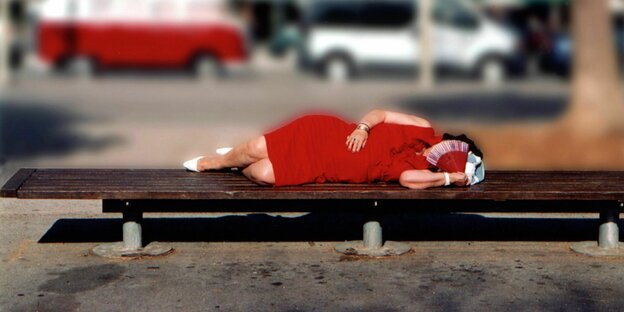 Das Foto zeigt eine Frau im roten Kleid, die auf einer Bank ruht.
