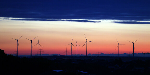 Windräder stehen unter einer Wolkenwand im Sonnenaufgang