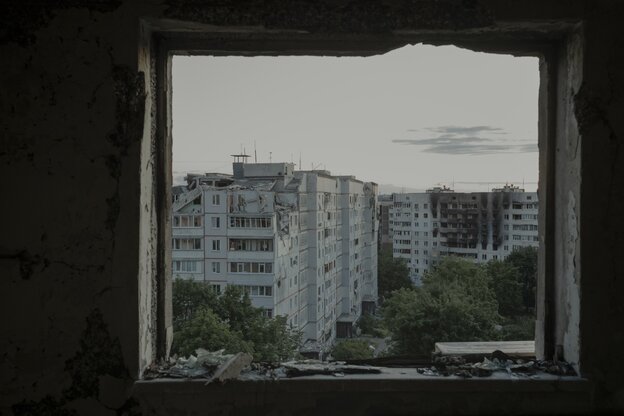 Blick durch ein offenes Fenster auf zerstörte Häuser in Kharkiv