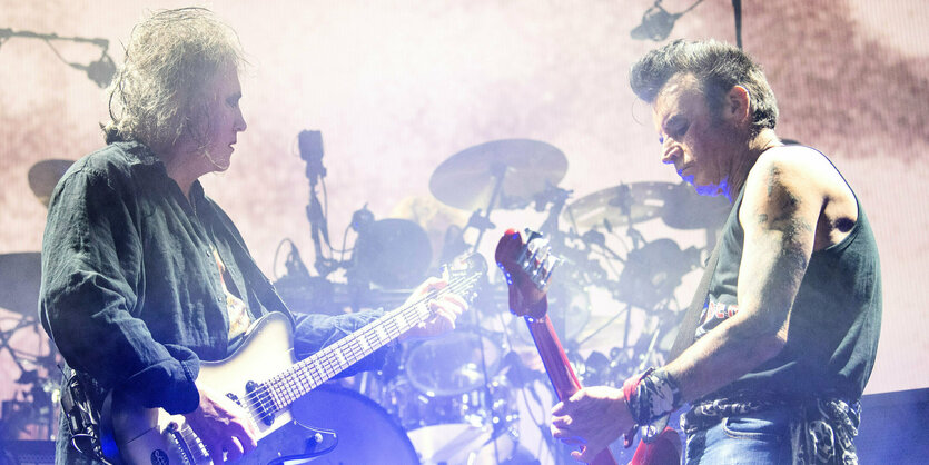 Robert Smith und Bassist Simon Gallup stehen auf der Bühne, im HIntergrund SChlagzeuger Jason Cooper