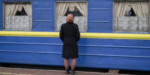 Eine Frau steht vor einem blau-gelben WAggon und nimmt Abschied