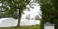 Weisse Zelte stehen auf einer Wiese unter Bäumen