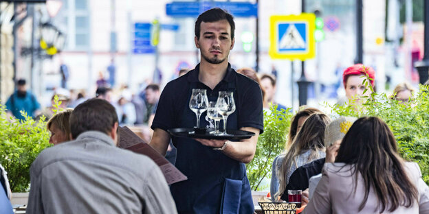 A waiter walks through the outside area of ​​a cafe with a tray