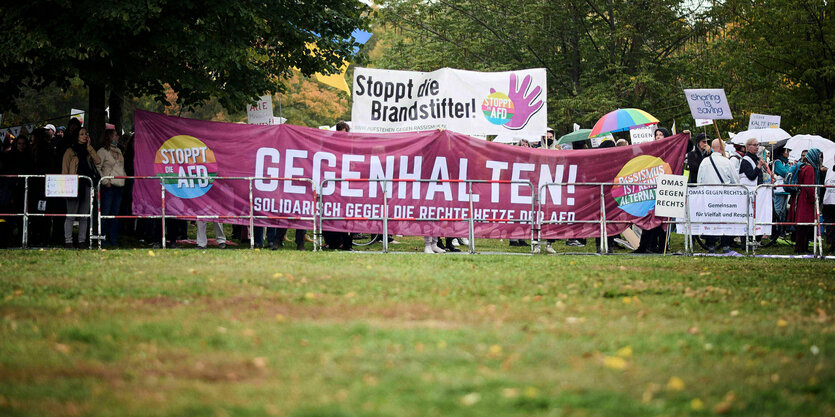 Protestaktion hinter einem Absperrgitter mit Transparenten auf denen steht: Gegenhalten ! oder Stoppt die Brandstifter