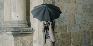 Eine Person hält sich einen Schirm vors Gesicht