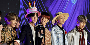 Sechs junge Männer stehen auf einer Bühne, einer trägt eine Geburtstagstorte als Hut