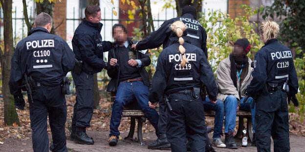 Schwarze sitzen im Görlitzer Park auf einer Bank und werden von Polizist*innen kontrolliert.