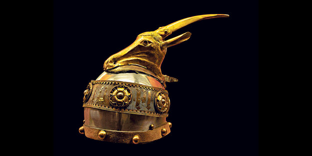 Der Skanderbeg-­Helm mit seinem Ziegenkopf auf vergoldeter Bronze vor schwarzem Hintergrund.