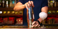 Zwei Hände halten einen Cocktailshaker in einer Bar