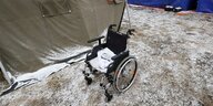 Ein schneebedeckter Rollstuhl steht zwischen den Zelten einer Notunterkunft für Geflüchtete