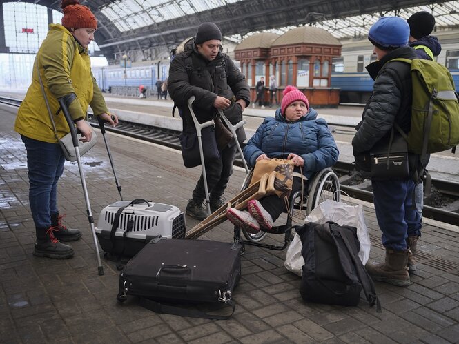 Eine Gruppe von Menschen auf einem Bahnsteig, jemand sitzt in einem Rollstuhl, zwei haben Krücken