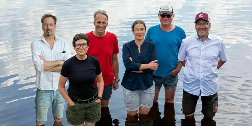 Zwei Frauen und vier Männer stehen mit kurzen Hosen im Wasser