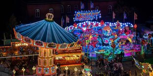 Der Bremer Freimarkt bei Nacht. Links im Vordergrund ein Kettenkarussel. Die Fahrgeschäfte leuchten mit bunten Lichtern und Reklameschriftzügen.