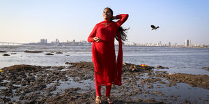 Eine Frau in einem roten Kleid am Meer vor der Silhoutte von Mumbai