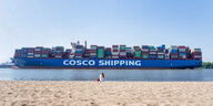 Voll beladendes Containerschiff mit der Aufschrift "Cosco Shipping", im Vordergrund Strand