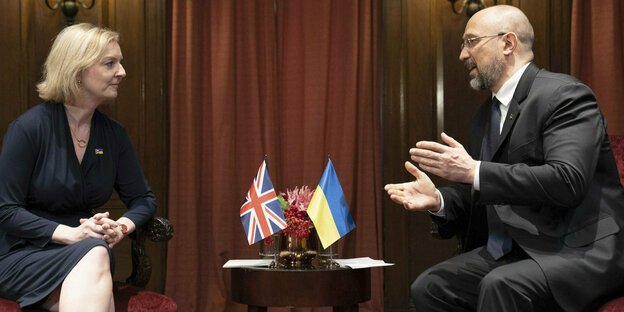 Liz Truss und der ukrainische Premier Minister Shmyhal sitzene sich gegenüber, dazwischen auf einem kleinen Tisch stehen die britische und die ukrainische Fahne