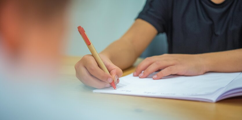 Ein Grundschüler sitzt an einem Tisch und schreibt mit einem Kugelschreiber in sein Heft