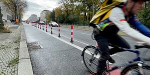 Radstreifen mit Poller auf Straße, Radfahrer fährt aus dem Bild