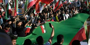 Demonstrierende halten gemeinsam eine große iranische Flagge auf der Demonstration