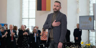 Ein Mann vor einem Publikum und einer Deutschlandfahne, er fasst sich symbolisch ans Herz