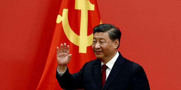 Chinas Staatschef Xi Jinping vor der Staatsflagge mit winkender Hand