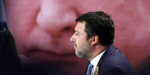 Matteo Salvini sitzt vor einem großen Putinfoto