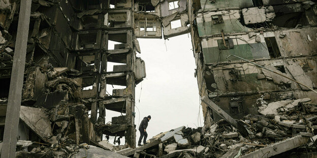 Ein Mann geht zwischen den Ruinen eines mehrstöckigen Hauses